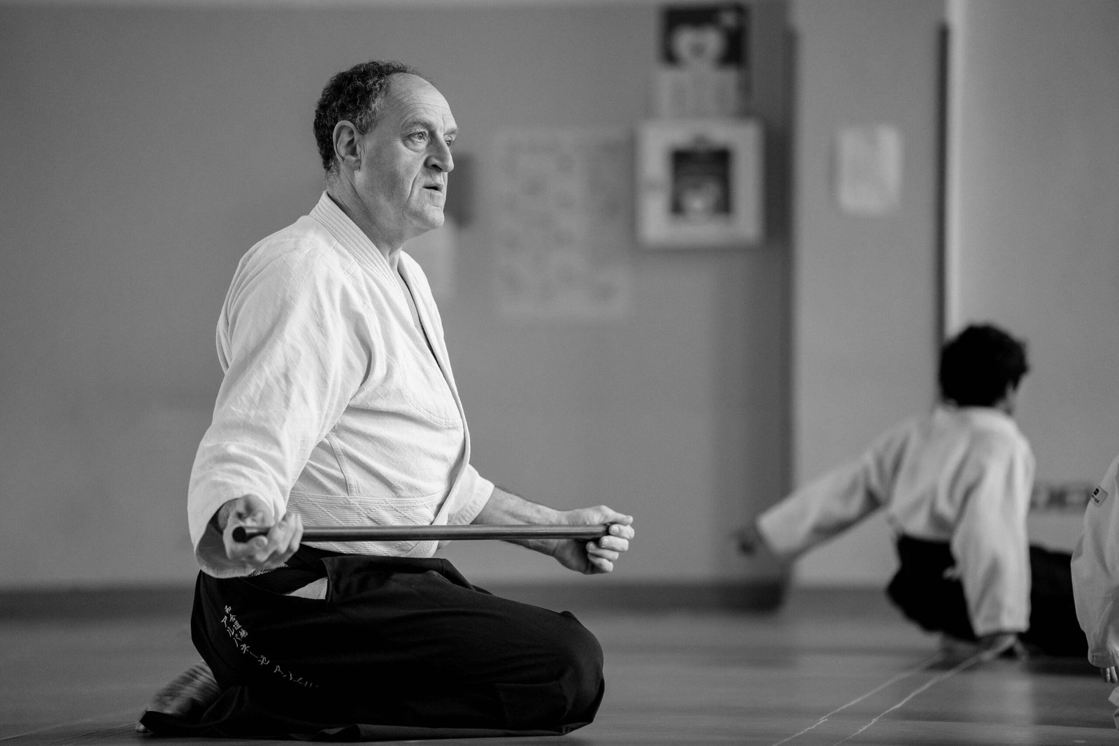Maestro in seiza con un bastone durante una lezione di Aikido in dojo, fotografia in bianco e nero